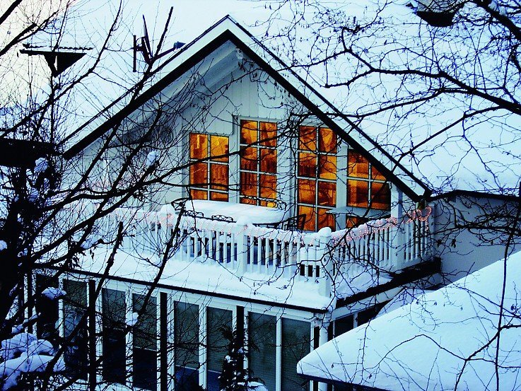 Eingeschneites Einfamilienhaus mit schneebedecktem Balkon und warm beleuchteten Fenstern
